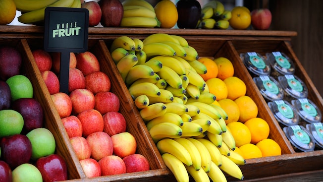 A fruit stand containing fresh apples, bananas, oranges and trail mix