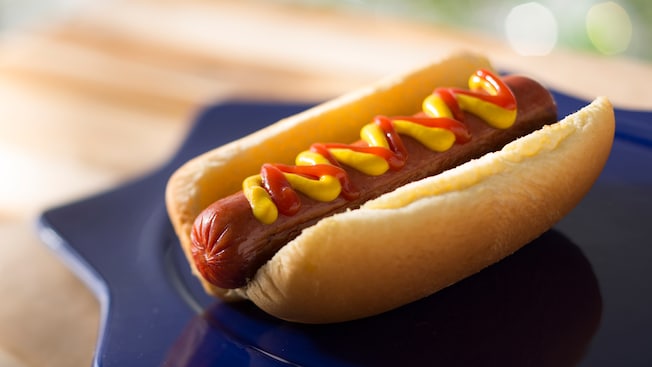 On a plate, a hot dog in a bun with ketchup and mustard
