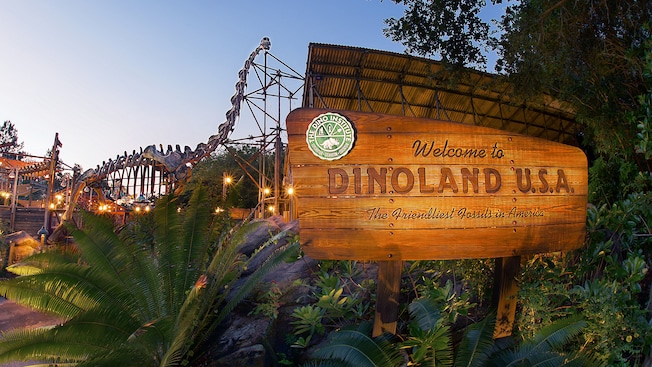 A wooden sign in front of dinosaur-themed attractions reads Welcome to Dinoland U.S.A.