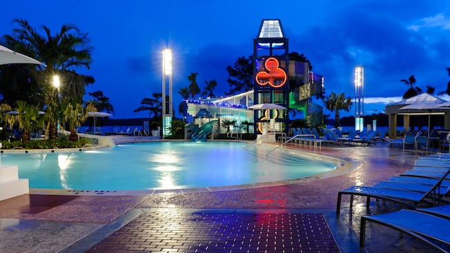 Nighttime view of a corner of Bay Cove pool, poolside lounge chairs, and a 20-foot high waterslide