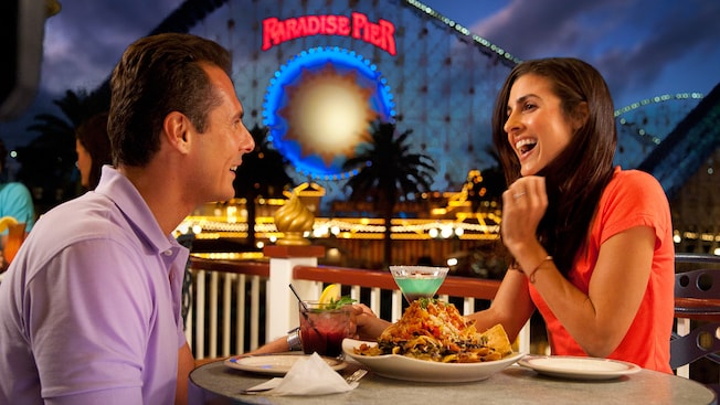 A couple enjoys drinks and food at Cove Bar near California Screamin' in Paradise Pier at night