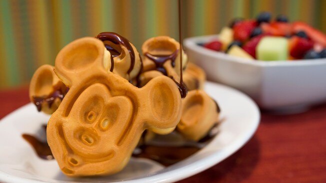 A plate of Mickey Mouse-shaped waffles drizzled with chocolate syrup