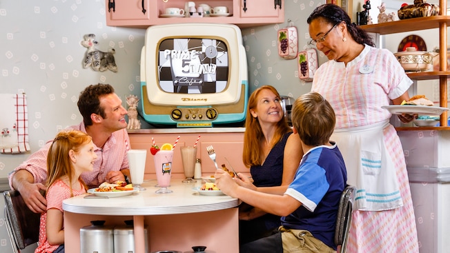 A Cast Member serves lunch to a family at 50's Prime Time Café
