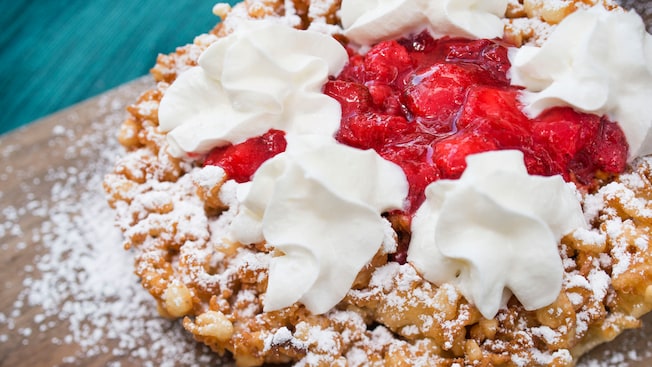 A close-up of a funnel cake topped with strawberries and whipped cream