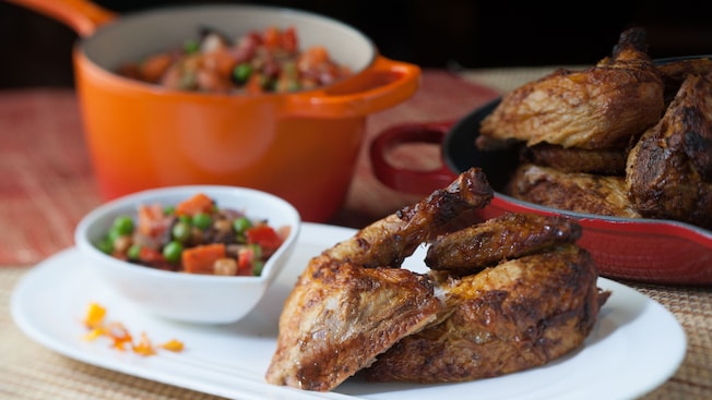 Oak-smoked rotisserie chicken on a plate with vegetables and, in the background, a pan with more chicken and a pot with more vegetables