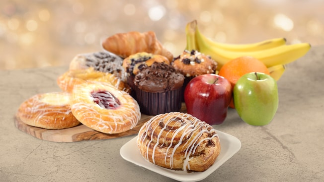 A collection of various pastries and muffins near bananas, apples and an orange