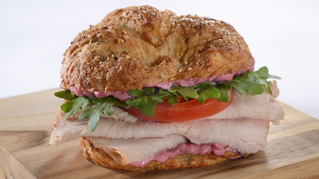 A multi-grain croissant sandwich stuffed with turkey, arugula and tomato