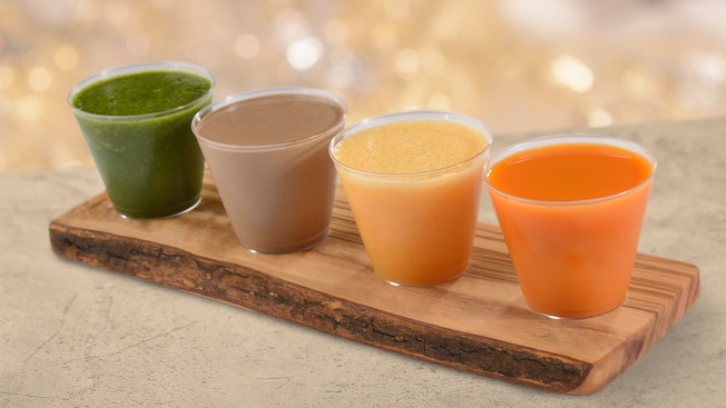 4 cups of different juices sit on a board