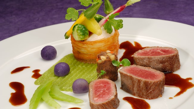 Slices of rare lamb artistically plated with miniature vegetables on a layer of celery puree 