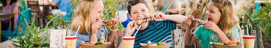 Three kids enjoy kabobs and beverages at an outdoor table